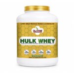 Hulk Whey protein powder in a white plastic jar with a gold lid, featuring a yellow honeycomb label, isolated on a white background.